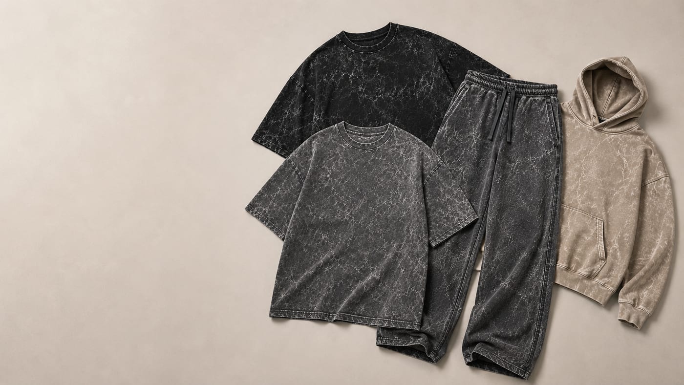 Acid wash collection flat lay — charcoal and black marbled tees, wide-leg sweatpants and a sand hoodie in PP-free vintage wash